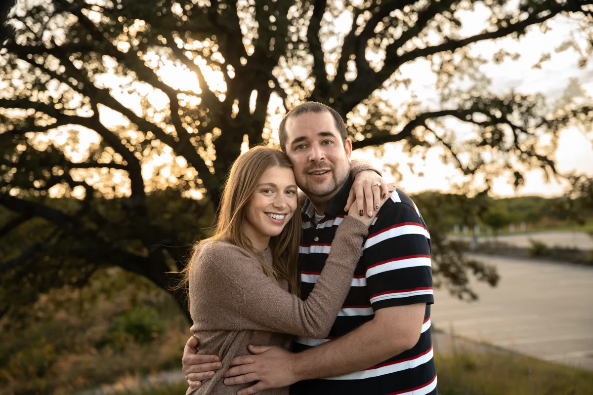 The newly engaged couple smiling together under a big oak in low golden light at Mahoney State Park, Nebraska
