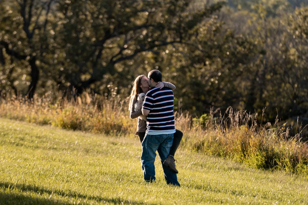 Seconds after the yes, she jumps into his arms in the open field at Mahoney State Park, Nebraska, photographed from across the field